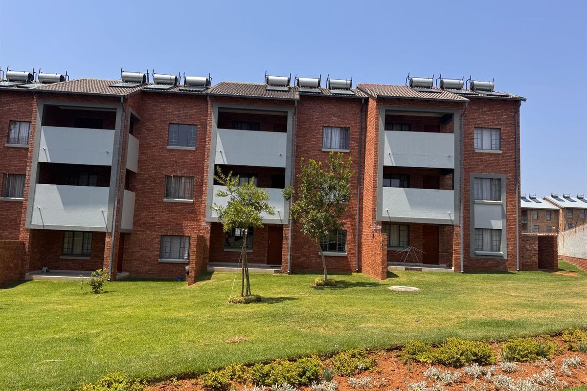 A well-maintained apartment complex featuring face brick architecture, private balconies, and solar water heating systems, set within a landscaped garden environment.