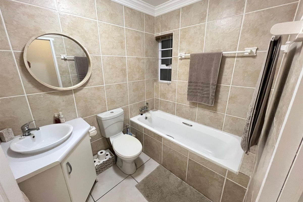 A well-maintained bathroom featuring neutral wall tiles, a built-in vanity with basin, a standard toilet, and a bathtub with shower mixer.