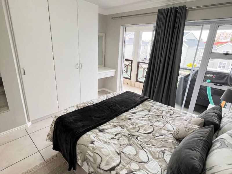 A well-maintained bedroom featuring built-in cupboards, a vanity, tiled flooring, and sliding glass doors providing access to an outdoor balcony area.