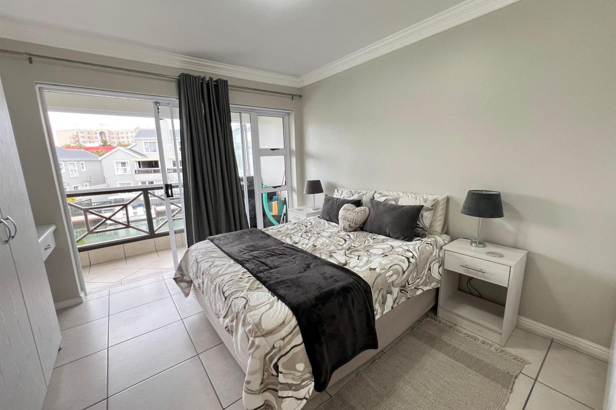 A well-maintained bedroom featuring tiled flooring, crown molding, and a sliding glass door providing direct access to a private balcony.