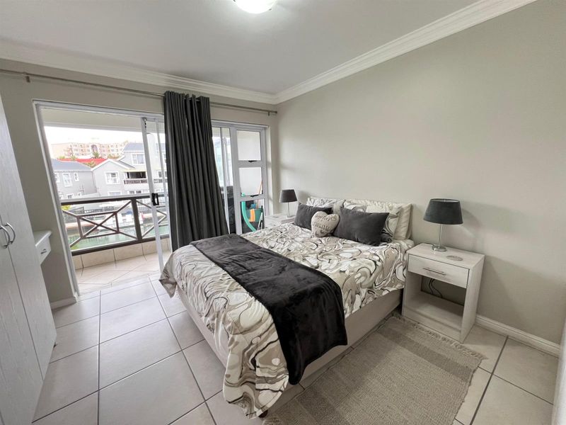 A well-maintained bedroom featuring tiled flooring, crown molding, and a sliding glass door providing direct access to a private balcony.