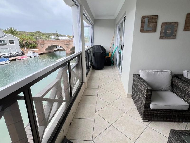 A covered balcony featuring tiled flooring and a glass balustrade, offering scenic views of the canal and bridge.