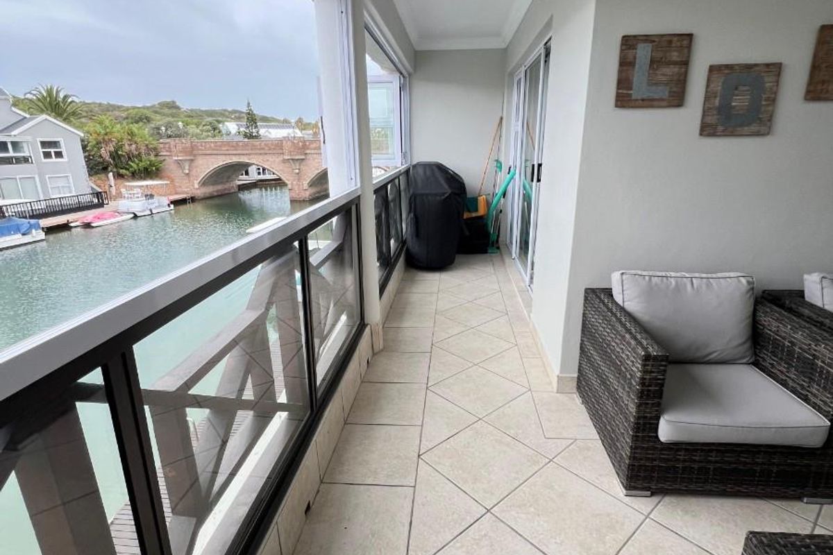 A covered balcony featuring tiled flooring and a glass balustrade, offering scenic views of the canal and bridge.