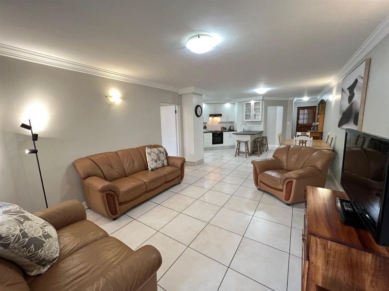 Spacious open-plan living and dining area featuring tiled flooring, crown molding, and a functional kitchen with built-in cabinetry and island.