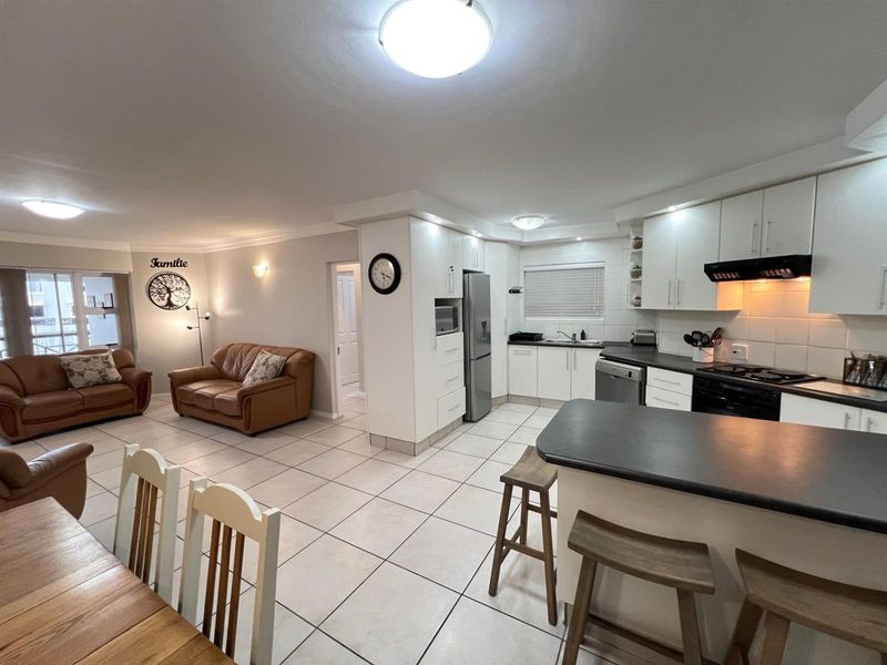 Spacious open-plan living area featuring a functional kitchen with built-in cabinetry, breakfast bar, and tiled flooring throughout the combined dining and lounge space.