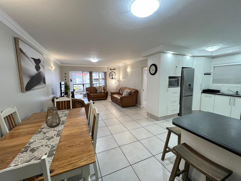 Spacious open-plan living and dining area featuring a modern kitchen with island, tiled floors, and sliding doors leading to an outdoor space.