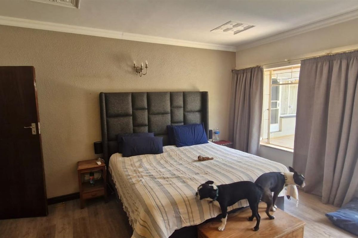 A bedroom featuring laminate flooring, coved ceiling details, and a wall-mounted light fixture, providing a functional space with natural light access.