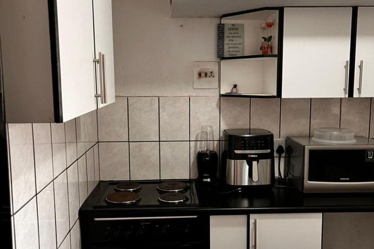A compact kitchen featuring black countertops, white cabinetry, a built-in electric stove, and tiled backsplash.