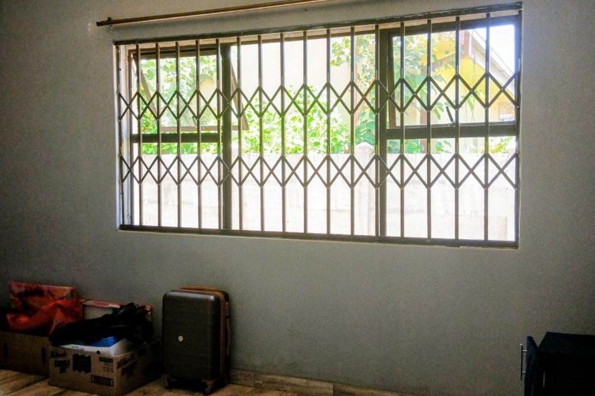 A bedroom featuring tiled flooring, a ceiling fan, and a window fitted with a security gate.