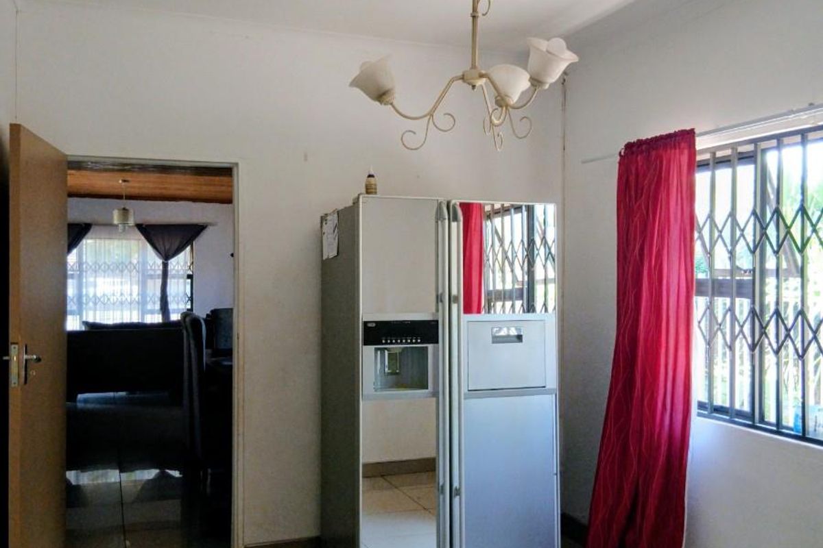 A functional kitchen area featuring tiled flooring, a decorative chandelier, and a security gate on the window, providing a clean and neutral space.