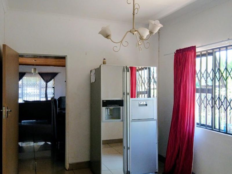 A functional kitchen area featuring tiled flooring, a decorative chandelier, and a security gate on the window, providing a clean and neutral space.