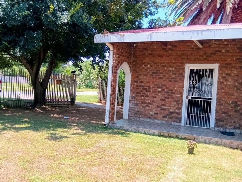 A view of the rear brick facade featuring a covered patio area, security gate, and established garden with mature trees.