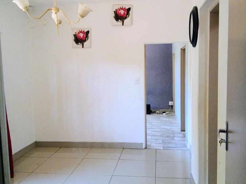 An empty living area featuring neutral tiled flooring and a decorative chandelier, providing a blank canvas for interior design.