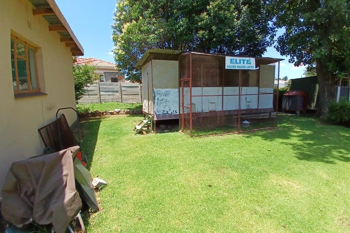 A rear garden area featuring a lawn and a large, weathered pigeon loft structure with metal mesh enclosure.