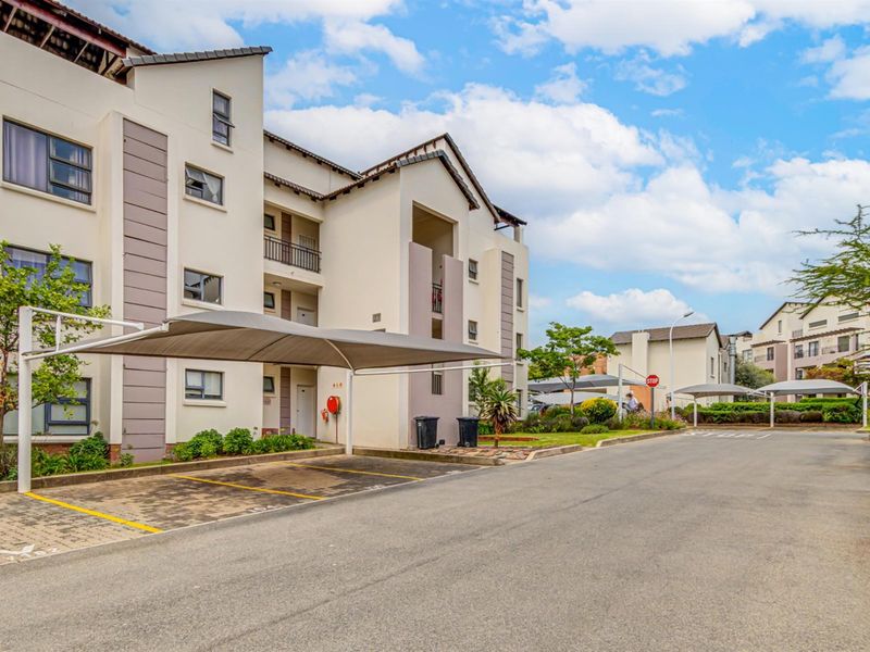 Exterior view of a modern apartment complex featuring covered parking bays, paved driveways, and well-maintained building facades with balconies.