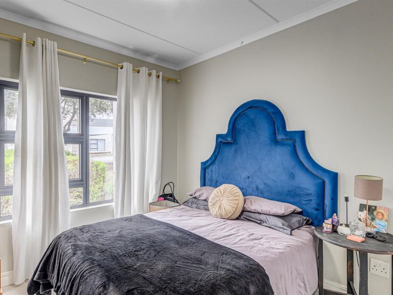 A well-lit bedroom featuring neutral wall tones, coved ceilings, and a large aluminium-framed window providing natural light.