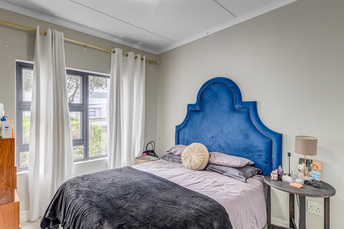 A well-lit bedroom featuring neutral wall tones, coved ceilings, and a large aluminium-framed window providing natural light.