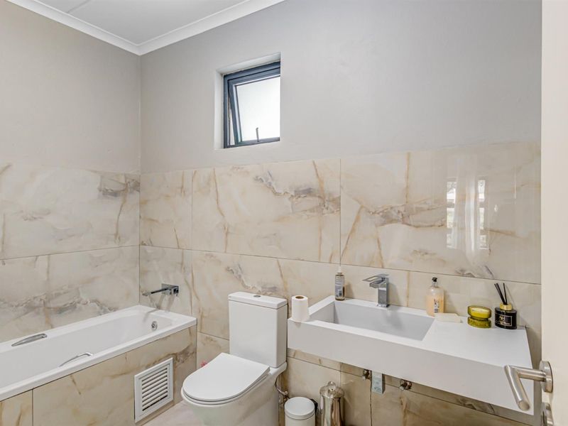 Modern bathroom featuring marble-look wall tiles, a wall-mounted vanity basin, and a built-in bathtub with contemporary chrome fixtures.