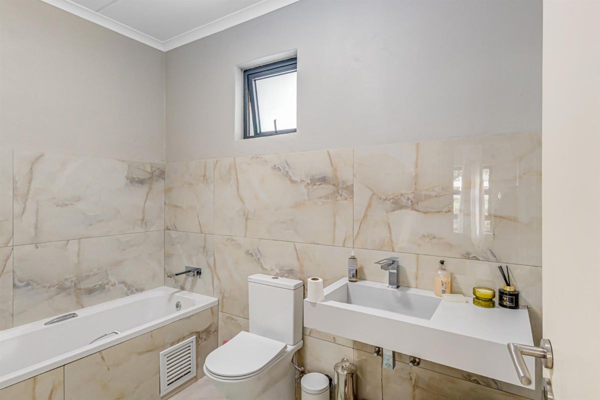 Modern bathroom featuring marble-look wall tiles, a wall-mounted vanity basin, and a built-in bathtub with contemporary chrome fixtures.