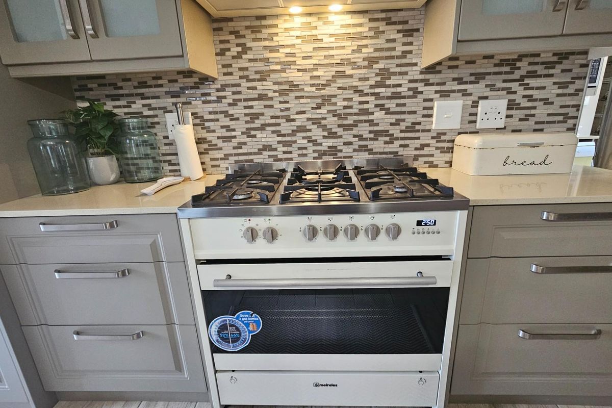 A modern kitchen featuring grey cabinetry, a mosaic tile backsplash, and a built-in gas stove with an integrated extractor fan.