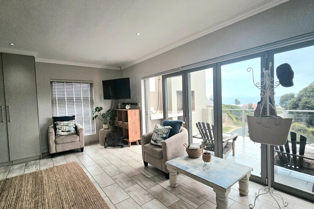 A bright living room featuring large sliding glass doors that open onto a balcony with scenic coastal views and modern tiled flooring.