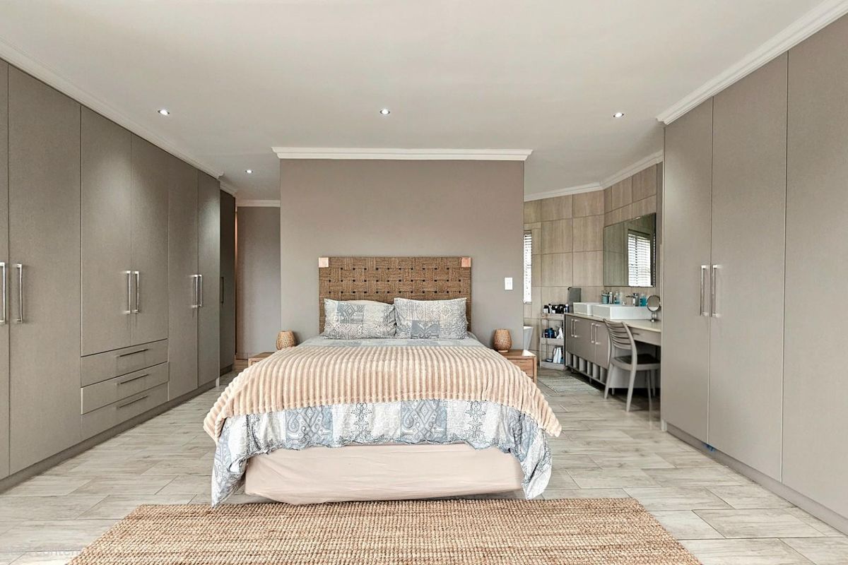 Spacious bedroom featuring extensive built-in cabinetry, neutral tiled flooring, and an integrated vanity area with modern finishes.