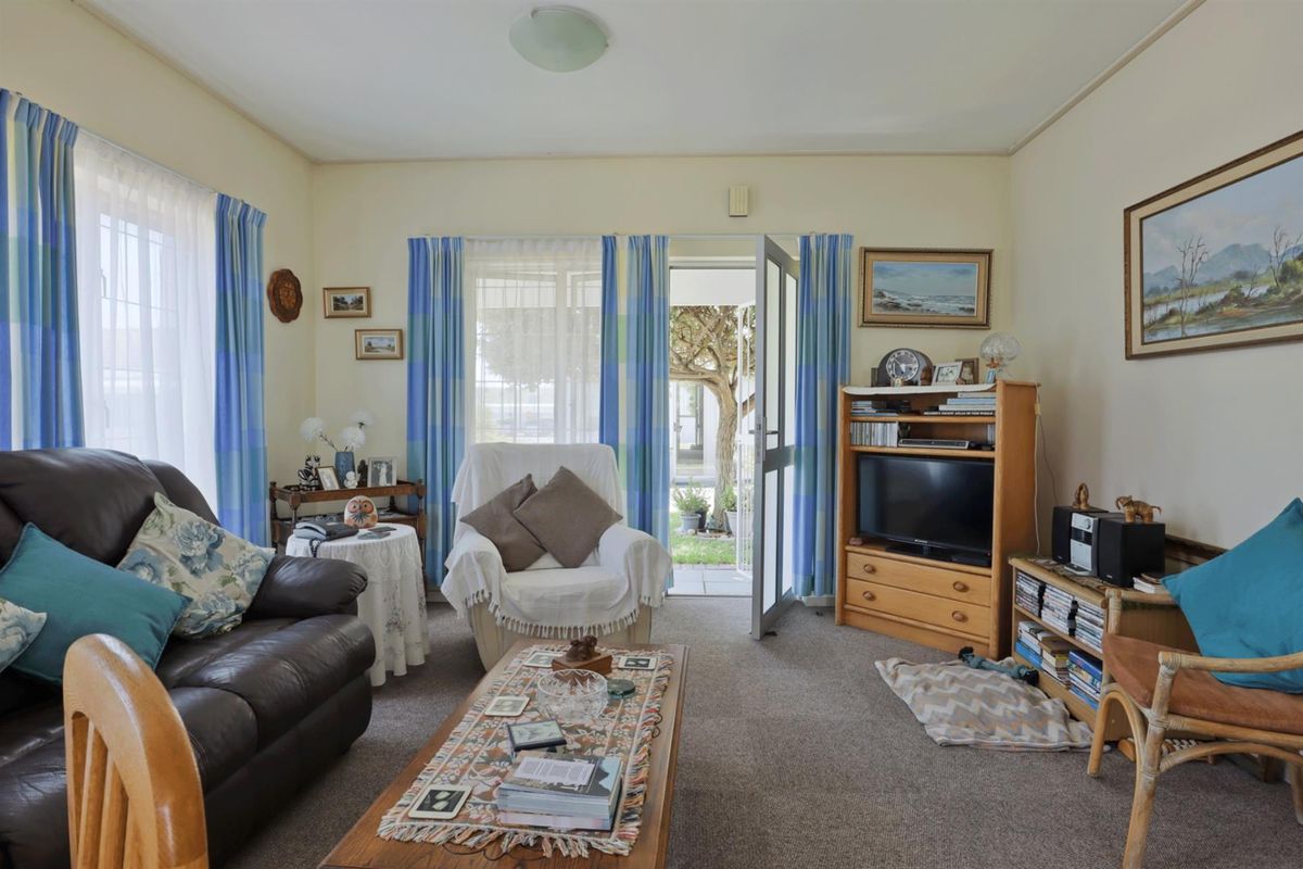 A comfortable living room featuring carpeted flooring, neutral walls, and a glass-panelled door providing direct access to the outdoor garden area.