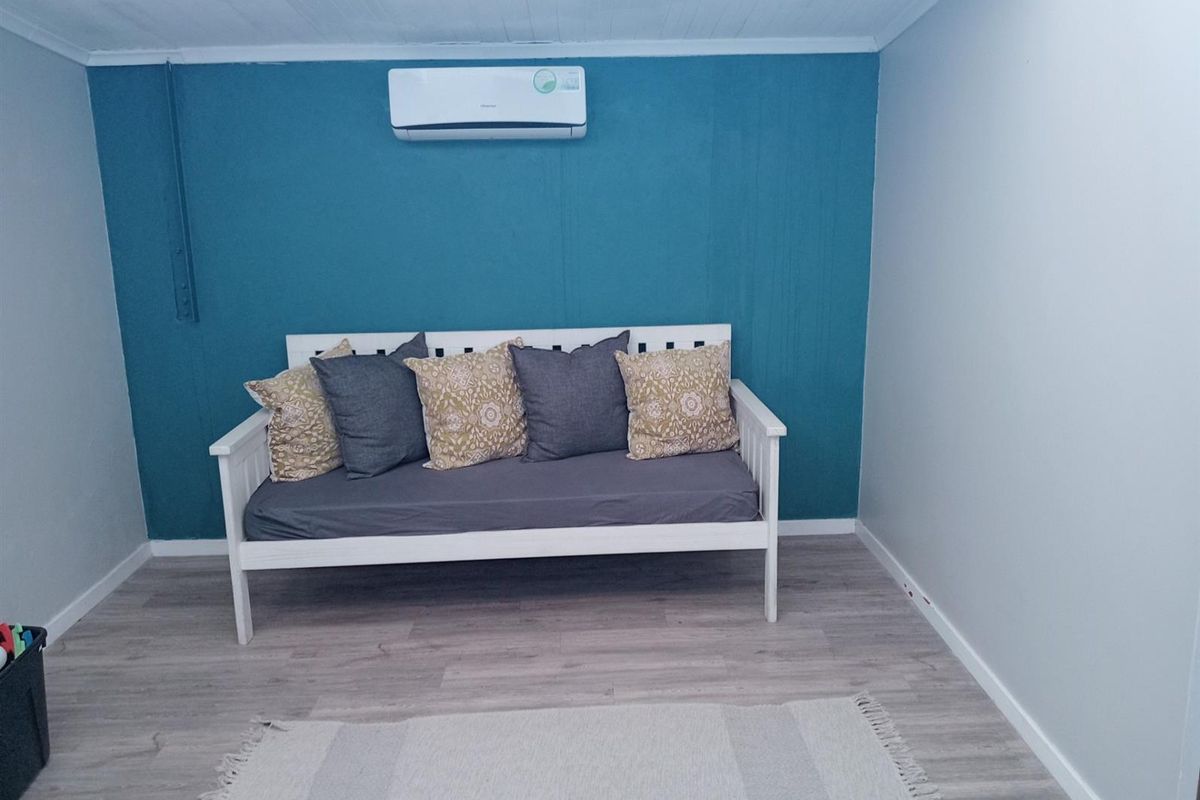 A simple interior room featuring light wood-look flooring, a blue accent wall, and a wall-mounted air conditioning unit.