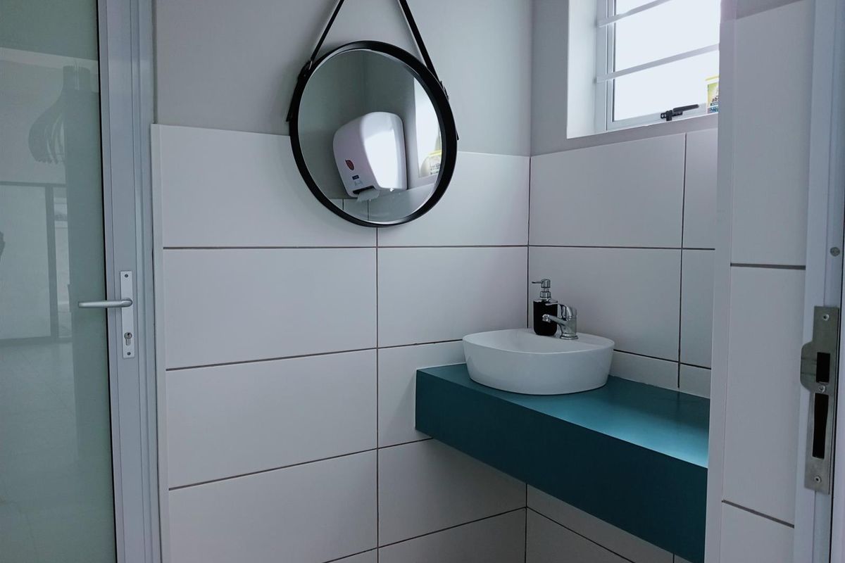 A clean, modern commercial restroom featuring a white vessel sink mounted on a teal floating vanity with tiled walls and a window.