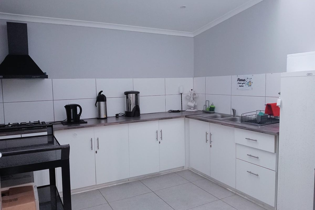 A functional commercial kitchen featuring white cabinetry, tiled splashbacks, a built-in extractor fan, and a double-basin stainless steel sink.