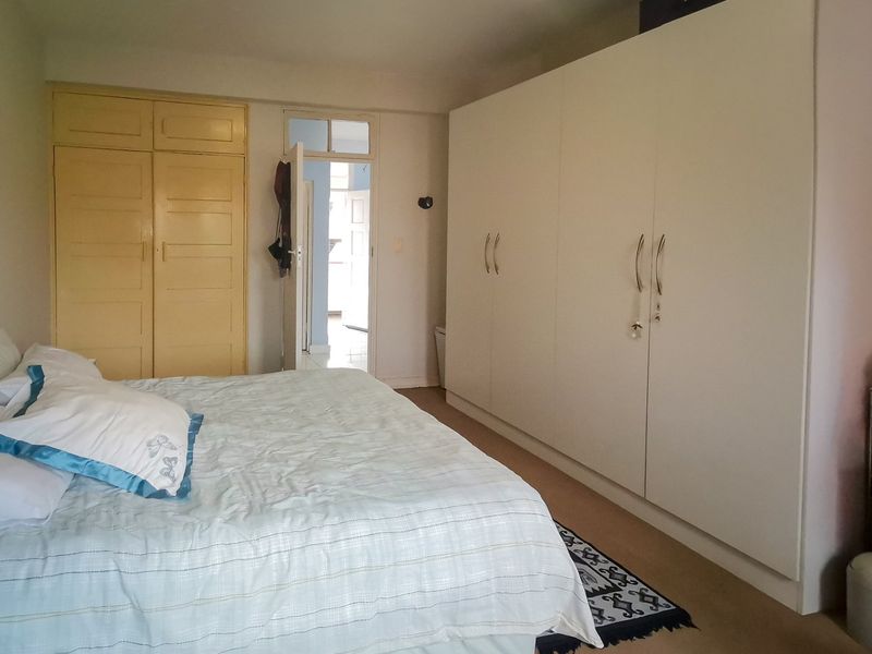 A spacious bedroom featuring extensive built-in cupboard storage and neutral finishes, offering a functional layout with direct access to the hallway.