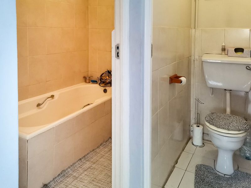 A dated bathroom featuring a separate bathtub area and a toilet with ceramic wall and floor tiling.