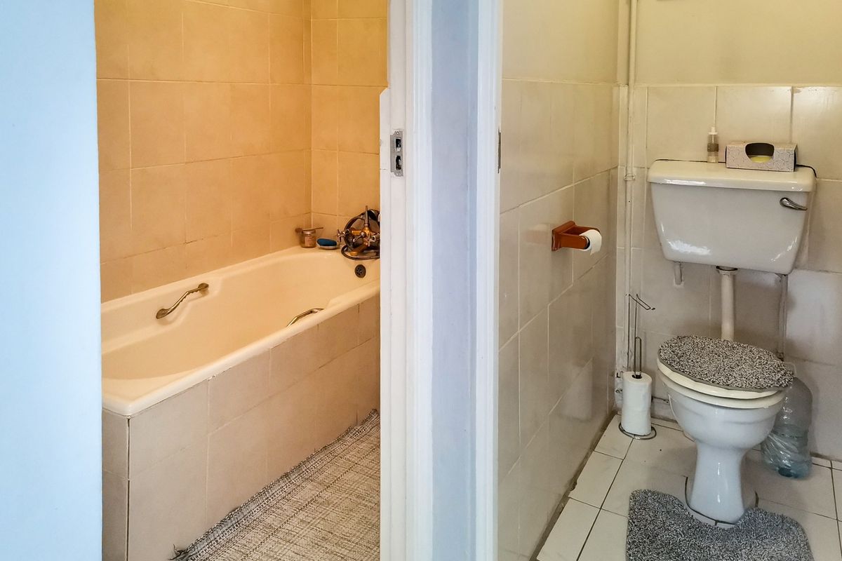 A dated bathroom featuring a separate bathtub area and a toilet with ceramic wall and floor tiling.