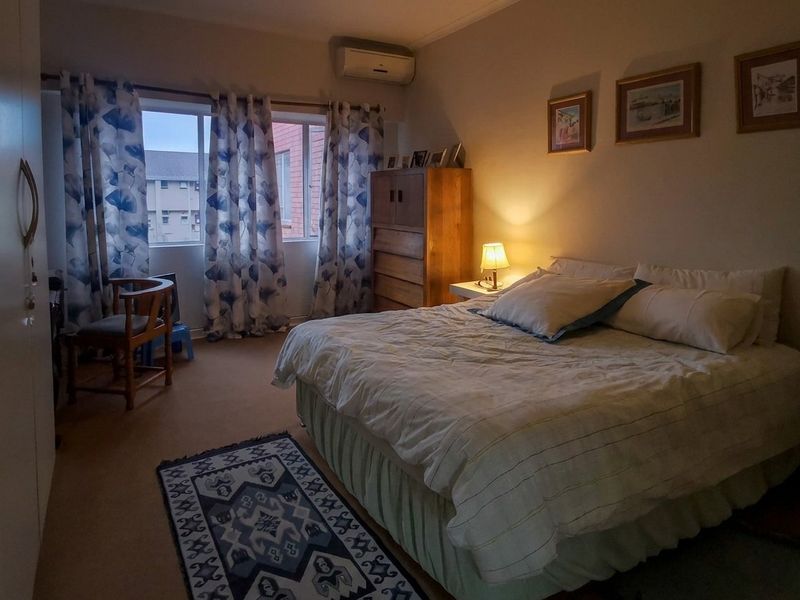 A comfortable bedroom featuring carpeted flooring, a built-in cupboard, and a wall-mounted air conditioning unit.