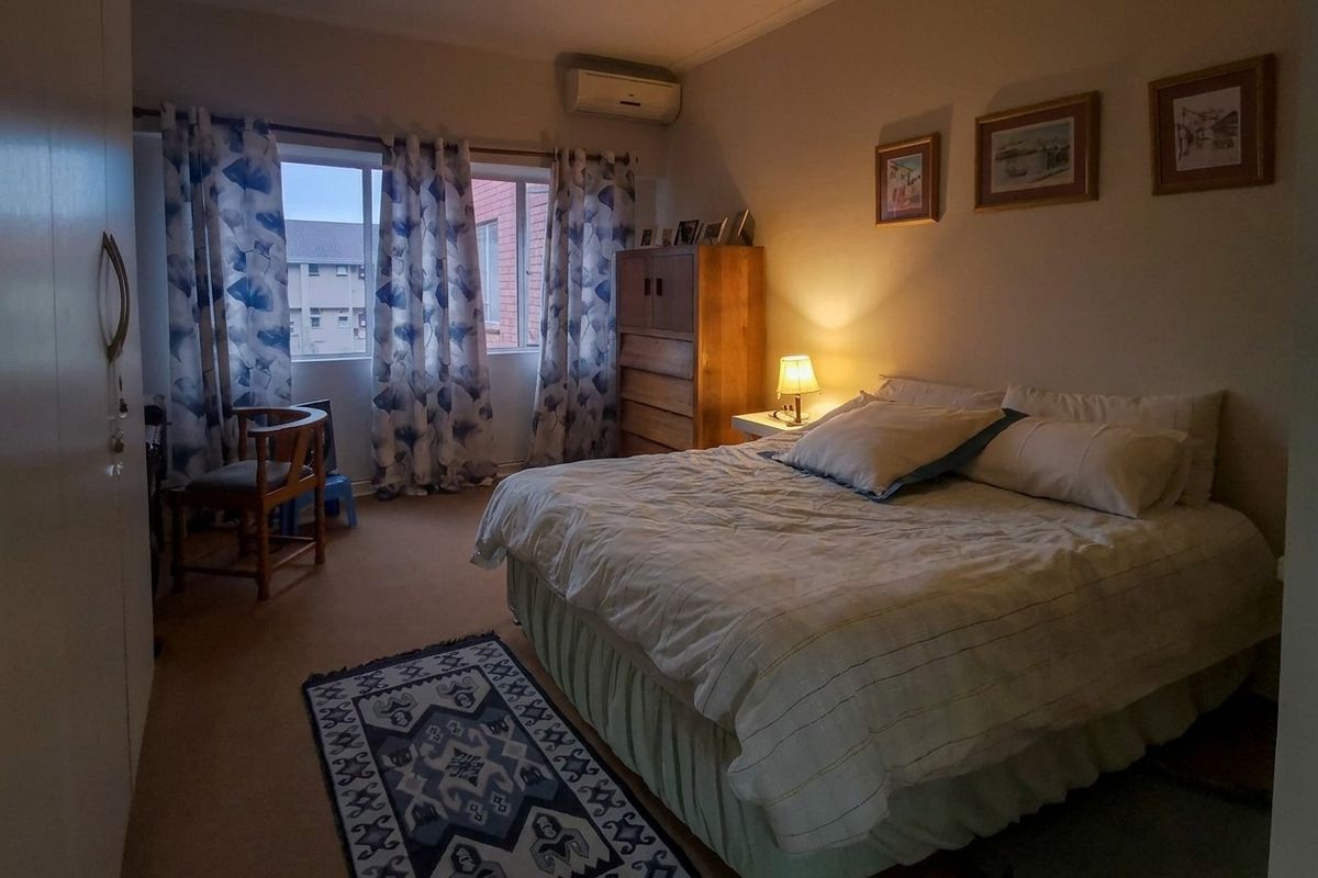 A comfortable bedroom featuring carpeted flooring, a built-in cupboard, and a wall-mounted air conditioning unit.