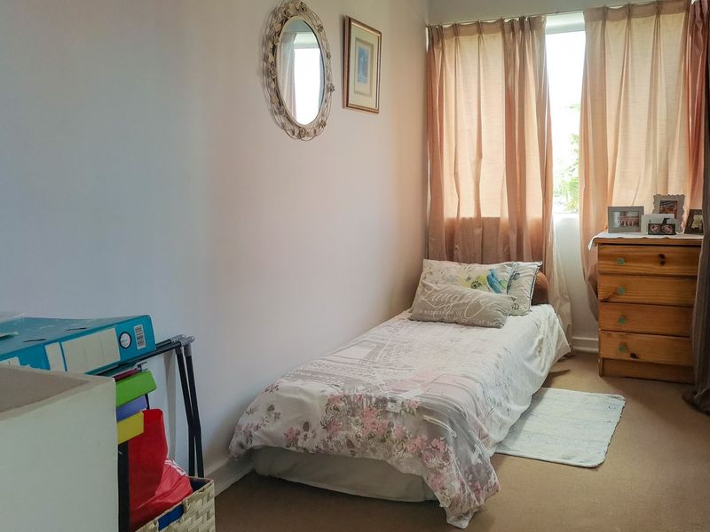 A compact bedroom featuring neutral wall finishes, carpeted flooring, and a window with curtains, providing a functional space for a single bed.