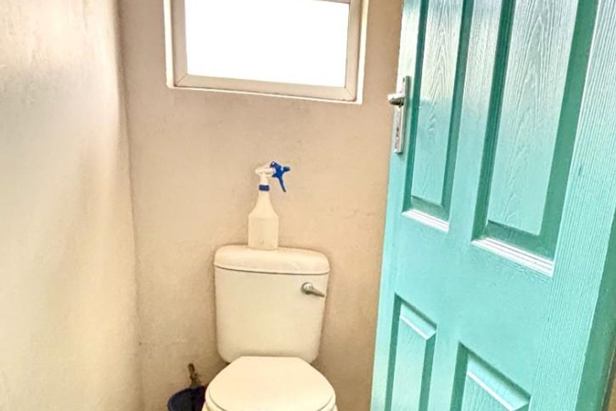 A small, functional bathroom featuring a standard toilet, window, and door, requiring cosmetic updates to improve the overall finish and appeal.