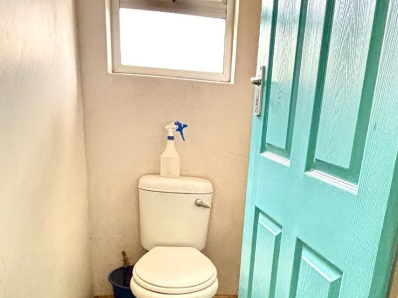A small, functional bathroom featuring a standard toilet, window, and door, requiring cosmetic updates to improve the overall finish and appeal.