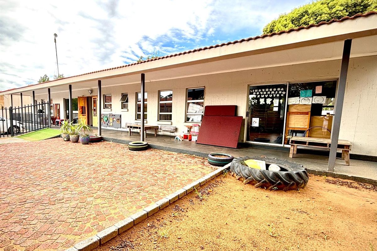 Exterior view of a commercial property featuring a covered patio area, paved ground, and sliding glass door access.