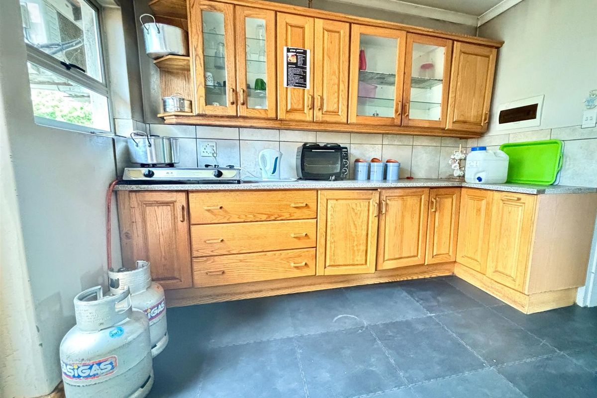 A dated kitchen featuring wooden cabinetry, tiled backsplash, and dark floor tiles, showing signs of wear and soot staining above the cooking area.