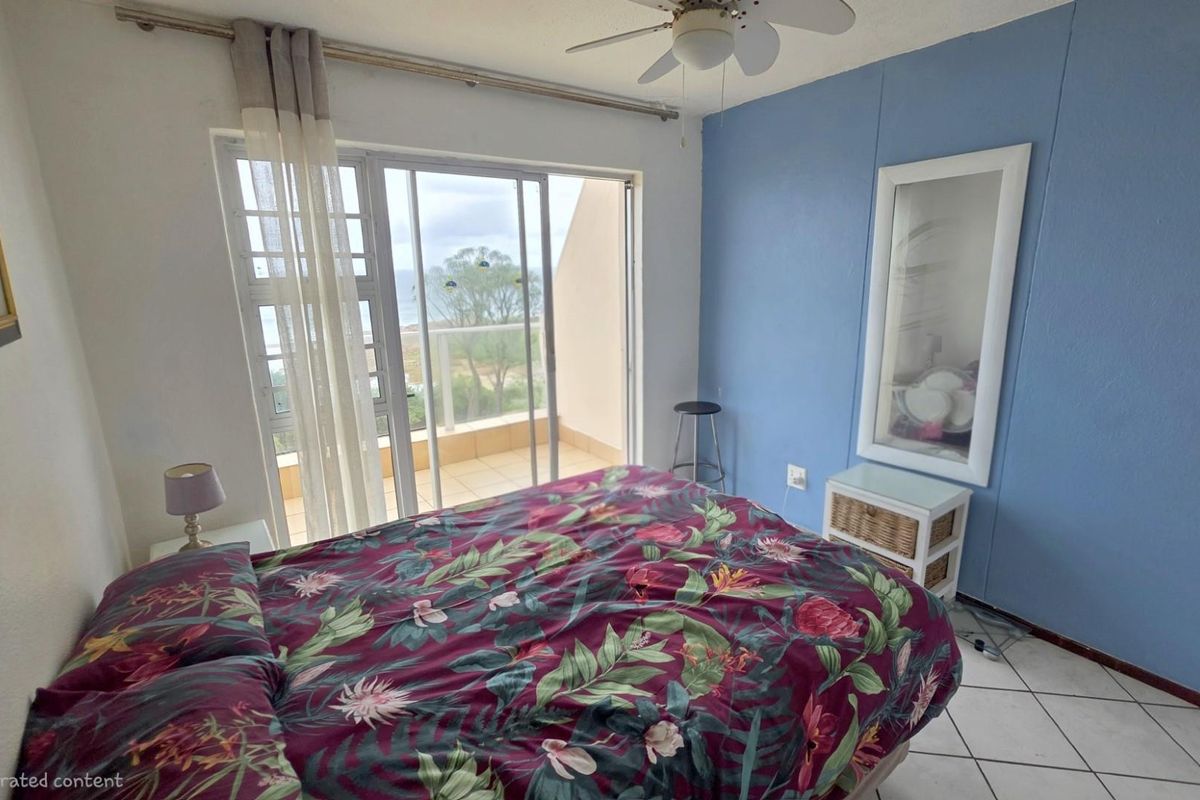A bedroom featuring tiled flooring, a ceiling fan, and sliding glass doors that open onto a private balcony with coastal views.
