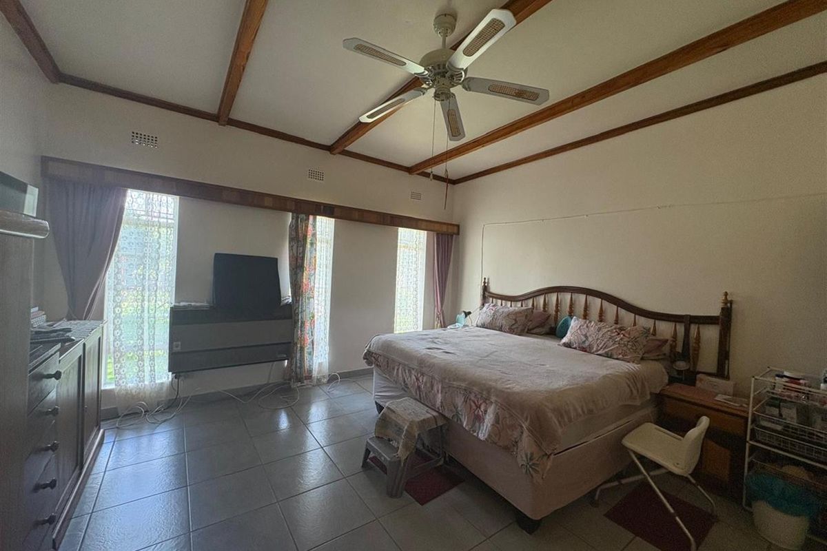 Spacious bedroom featuring tiled flooring, exposed timber ceiling beams, and a ceiling fan, offering a functional layout with natural light.