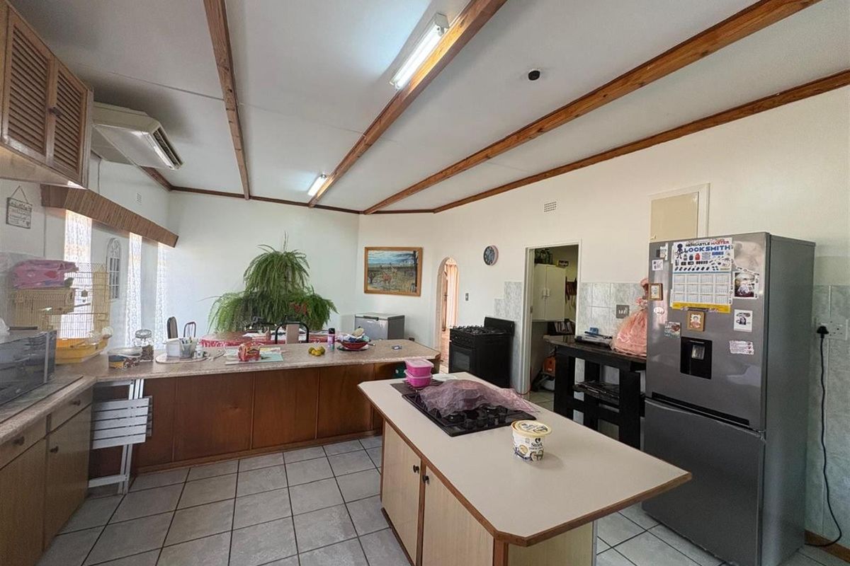 Spacious kitchen featuring a central island with built-in hob, ample cabinetry, and tiled flooring, offering a functional layout with potential for modernization.