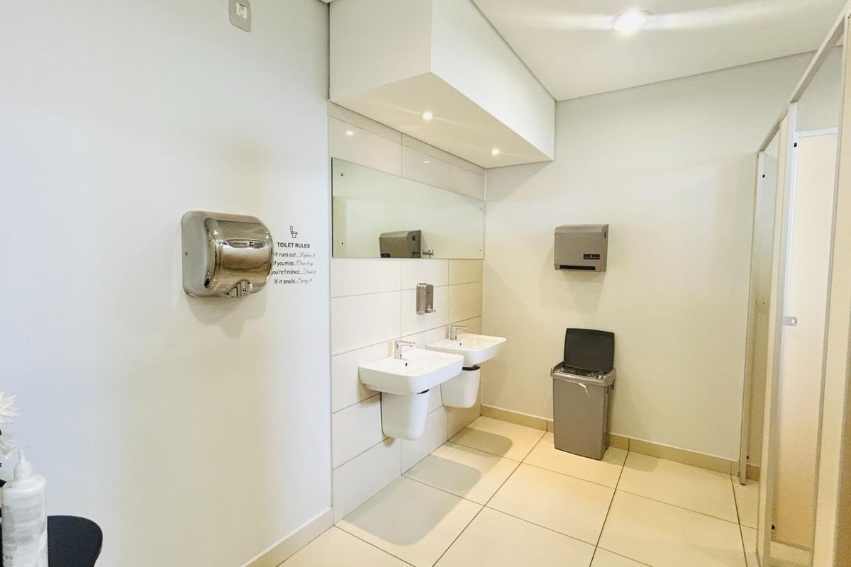 A clean commercial restroom featuring dual wall-mounted basins, a large vanity mirror, stainless steel hand dryer, and tiled flooring.