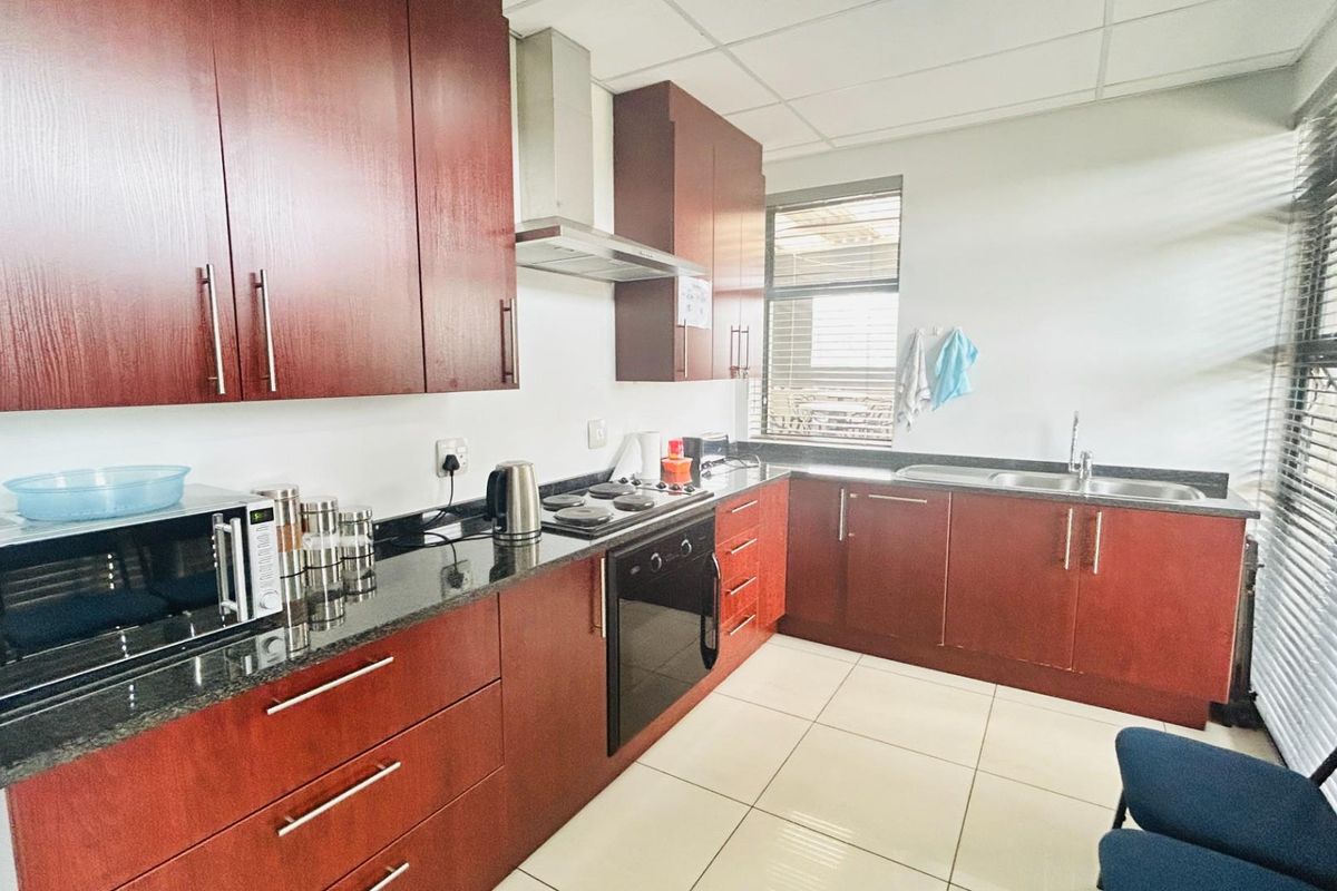 A functional commercial kitchen featuring dark wood cabinetry, granite countertops, a built-in oven, hob, extractor fan, and a double stainless steel sink.