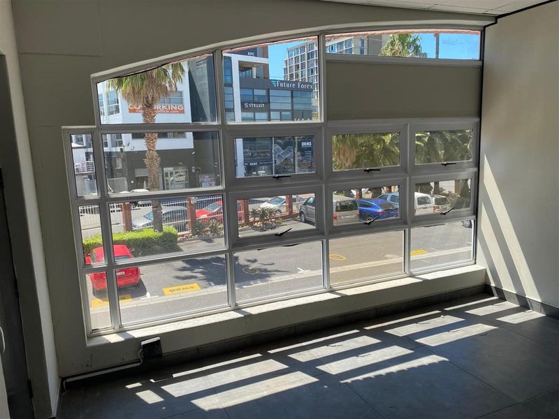 A bright, empty office space featuring large aluminium-framed windows that provide ample natural light and a view of the street.