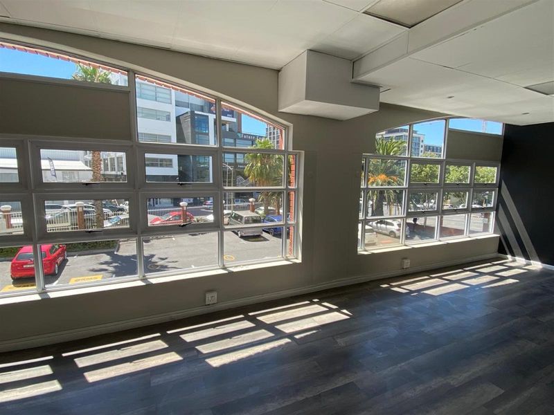 Bright open-plan retail or office space featuring large windows with street views, laminate flooring, and a suspended ceiling.