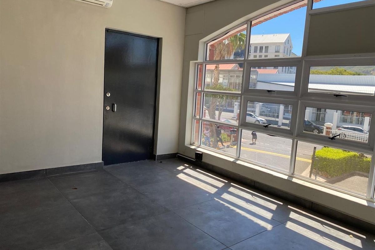 A bright, open-plan retail space featuring large windows, tiled flooring, and a wall-mounted air conditioning unit, offering excellent natural light and street visibility.