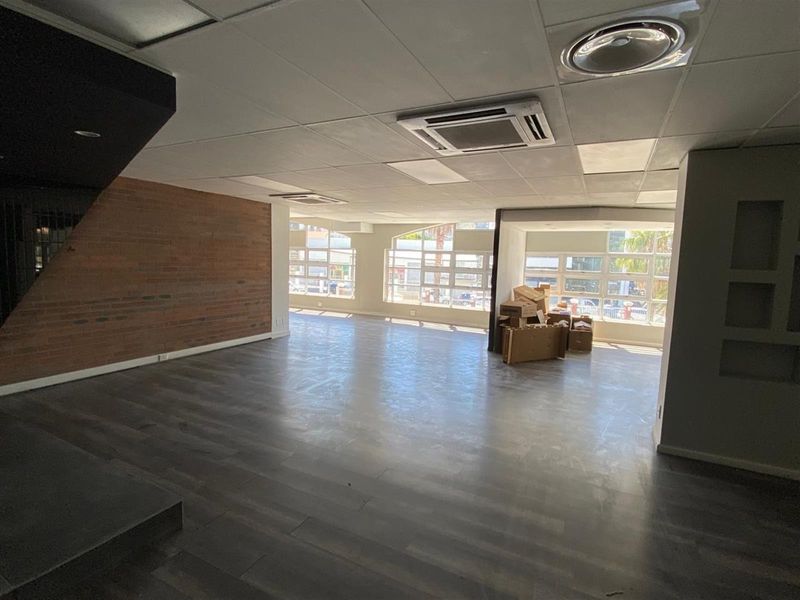 Spacious open-plan retail area featuring exposed brick accents, modern laminate flooring, suspended ceilings with integrated air conditioning, and large windows providing ample natural light.