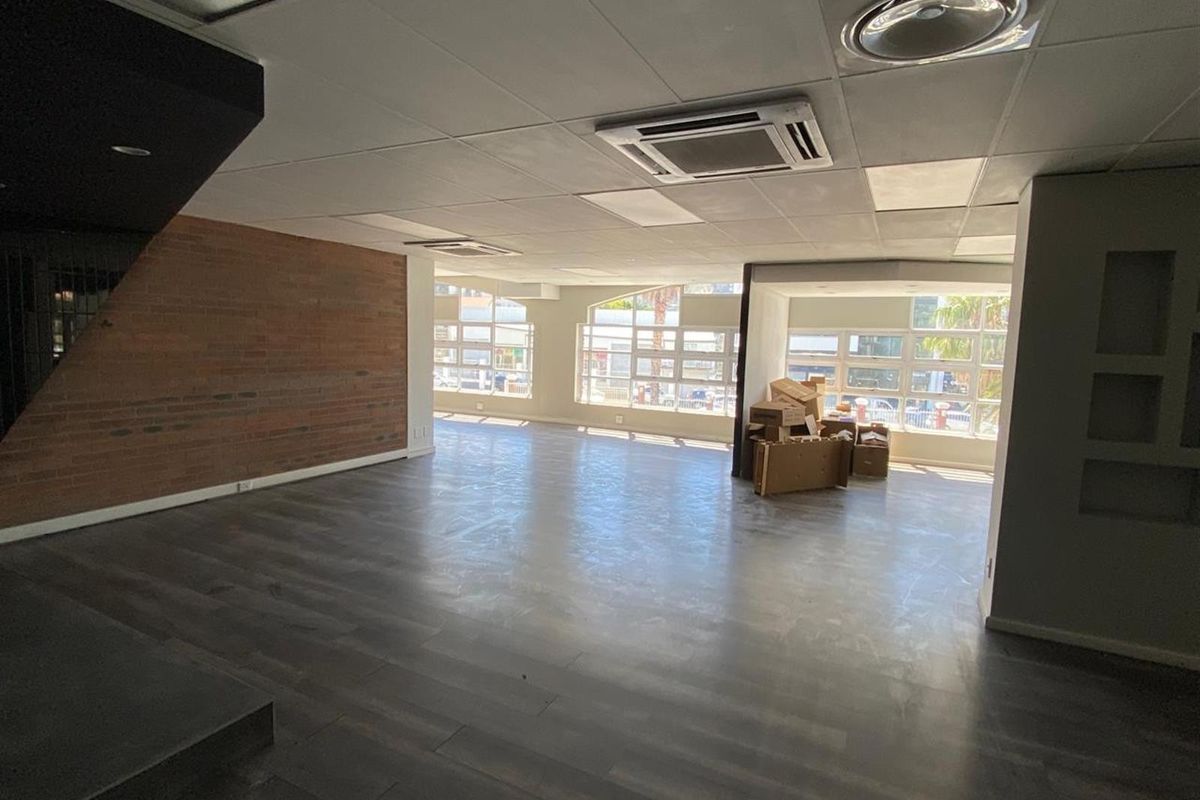 Spacious open-plan retail area featuring exposed brick accents, modern laminate flooring, suspended ceilings with integrated air conditioning, and large windows providing ample natural light.